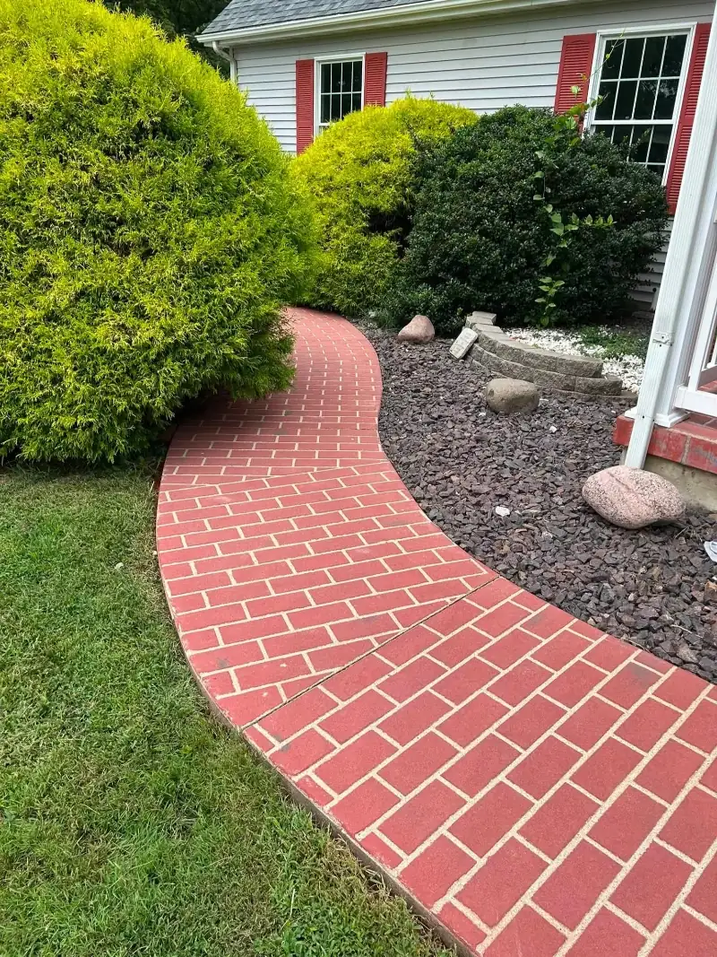 Curved red brick walkway with faded, moss-stained pavers before pressure washing in Asheville, NC